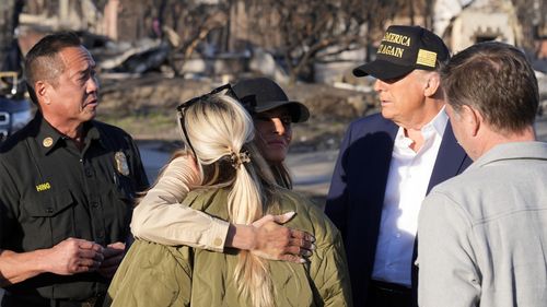 President Donald Trump watches as first lady Melania Trump hugs a resident, as they tour the Pacific Palisades neighborhood affected by recent wildfires in Los Angeles, Friday, Jan. 24, 2025. (AP Photo/Mark Schiefelbein)