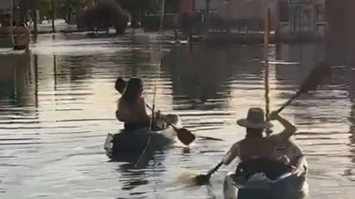Two women paddle kayaks in Forbes after major flooding in NSW.