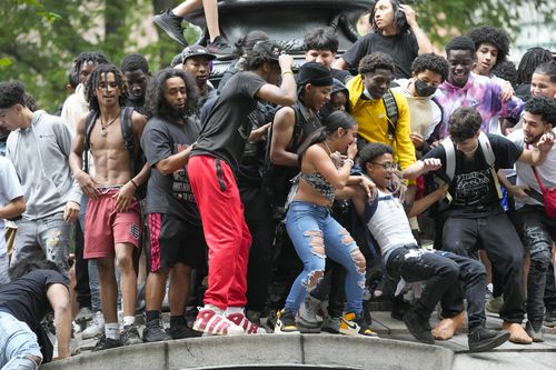 People dance after climbing on a sculpture, Friday, Aug. 4, 2023, in New York's Union Square. 