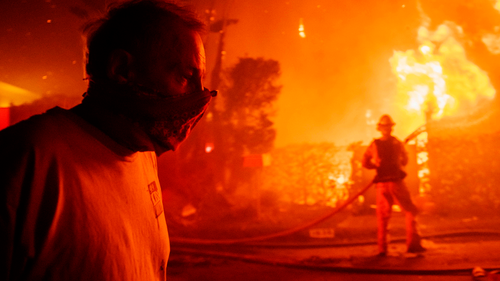 A man walks past a burning home during the Getty fire, Oct. 28, 2019, in Los Angeles, Calif. (AP Photo/ Christian Monterrosa)