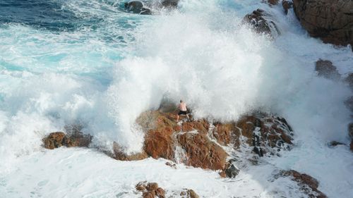 The man on the rocks moments before he was swept off.