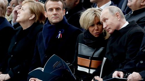 Russian President Vladimir Putin and French First Lady Brigitte Macron talk as they sit alongside French President Emmanuel Macron and German Chancellor Angela Merkel.