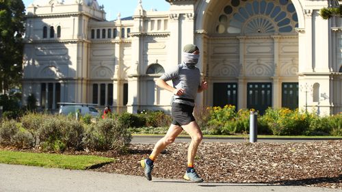 A man wearing a face cover runs through the Carlton Gardens in Melbourne, Australia