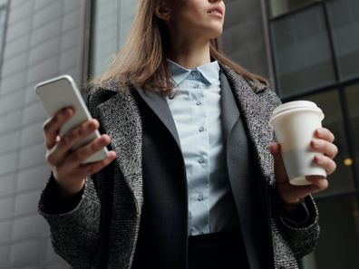 Stock photo of a successful business woman holding phone and coffee.
