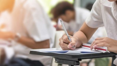 Exam at school with student's taking educational admission test in class, thinking hard, writing answer in university classroom, education and world literacy day concept