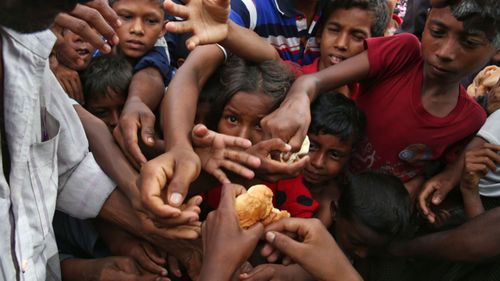 Rohingya children stretch their hands out to receive food distributed by locals at a makeshift refugee camp in Bangladesh. (AAP)