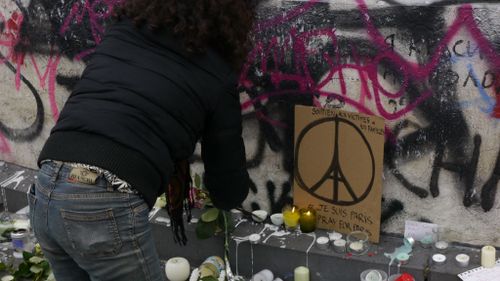 A woman lights a candle near a Parisian peace sign at Place de la Republique. (9NEWS)