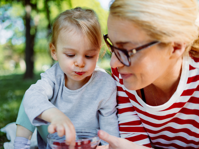 Toddler eating in the park with mum. 