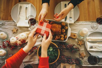 Two female friends exchanging gifts at the decorated Christmas table