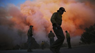 U.S. Forest firefighters stand along Triangle Road watching a wildfire called the Oak Fire burn east of Midpines in Mariposa County, Calif., Friday, July 22, 2022. The fast-moving wildfire near Yosemite National Park erupted Friday afternoon and prompted evacuations even as firefighters made progress against an earlier blaze that burned to the edge of a grove of giant sequoias. (Eric Paul Zamora/The Fresno Bee via AP)