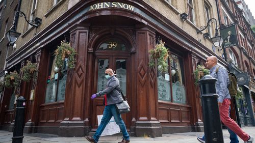 A person wearing a protective face mask walks past a temporarily closed pub named after the founding father of epidemiology John Snow, on June 19, 2020 in London, England.