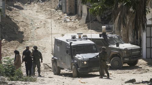 Israeli soldiers speak with Palestinians in the West Bank urban refugee camp of Tulkarm while residence evacuate their homes and carry their belongings as the Israeli military continues its operation in the area ahead of planned home demolitions by Israeli security forces, Sunday, July 6, 2025. (AP Photo/Majdi Mohammad)