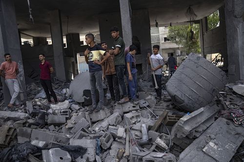 Palestinians stand by buildings destroyed in Israeli bombardment in Rafah refugee camp in Gaza Strip on Tuesday, Oct. 17, 2023 
