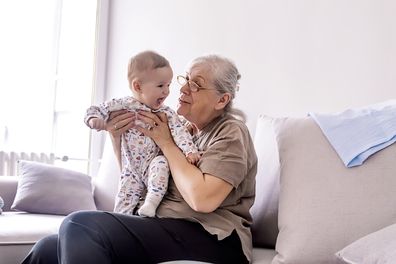 Grandmother holding little grandson in the room at home. Senior woman hold little baby cute smiling. Happy grandmother with her grandchild in home.