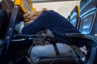 A woman leaning over on an airplane seat table to rest and sleep on a Ryanair flight within Europe.