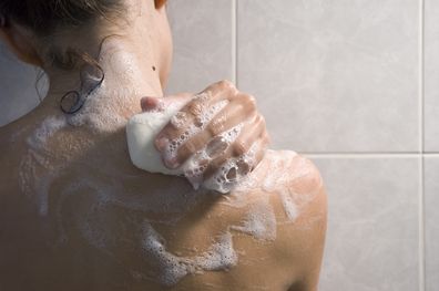 Woman washing her back in the shower with soap