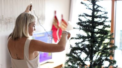 Woman stringing lights onto a christmas tree