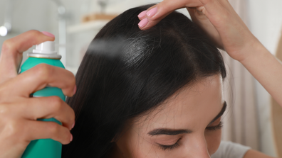 Girl sprays dry shampoo on her hair. 