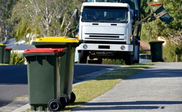 Focus on two Rubbish bins with rubbish truck in background lifting a bin