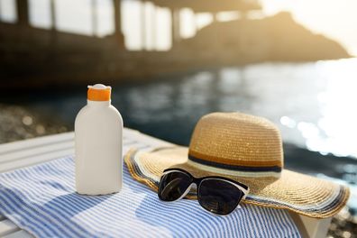 Suntan cream bottle and sunglasses on beach towel with sea shore on background. Sunscreen on deck chair outdoors on sunrise or sunset. Skin care and protection concept.