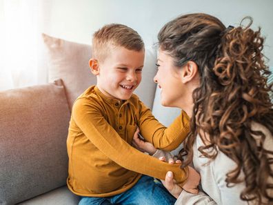 A mother and son sitting on a couch and smiling at each other.