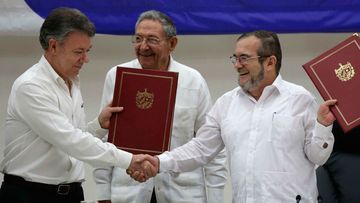 Colombian President Juan Manuel Santos, left, and Commander of the Revolutionary Armed Forces of Colombia or FARC, Timoleon Jimenez, right, shake hands during a signing ceremony of a cease-fire and rebel disarmament deal, in Havana, Cuba. (AAP)