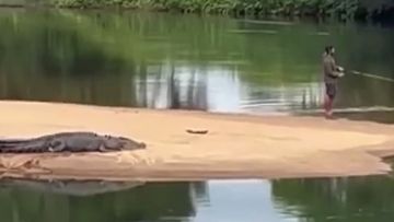A man has been filmed fishing as a croc lays metres behind him on a riverbank near Cairns.