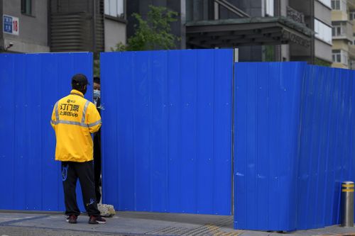 A delivery worker chats with a masked security guard at a barricaded fence of a locked-down residential complex.