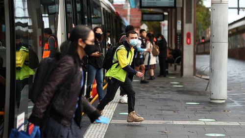 Pasażerowie w maskach wysiadają z tramwaju na dworcu centralnym w Sydney.