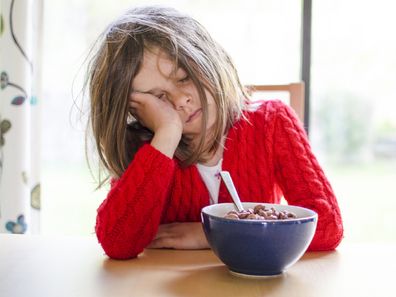 Tired mother, trying to pour coffee in the morning with cereal