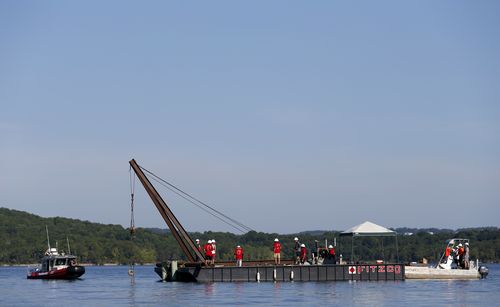 Using a barge mounted crane, a salvage crew from Fitzco Marine Group begin the process of raising a duck boat from below the surface of Table Rock Lake, near Branson, Mo., on Monday, July 23, 2018. 17 people were killed last week when the duck boat sank. (Nathan Papes /The Springfield News-Leader via AP)