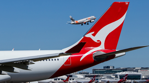 Qantas aircraft on tarmac and Jetstar plane flying in the background