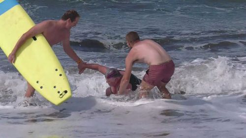 Surfers help Judy to her feet after she became distressed off an Adelaide beach.