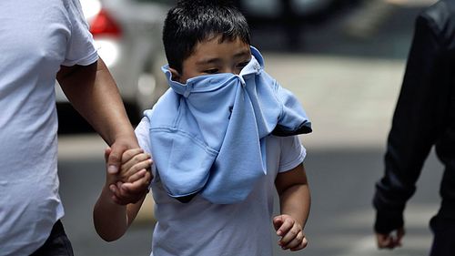 A boy with his face covered due to a gas leak holds aman's hand as people gather in Reforma Avenue after an earthquake in Mexico City. (AAP)