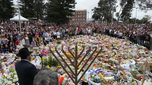 Rabbi Motti Feldman, lower left, speaks at a menorah lighting ceremony at a floral memorial for victims of Sunday's shooting, at the Bondi Pavilion.