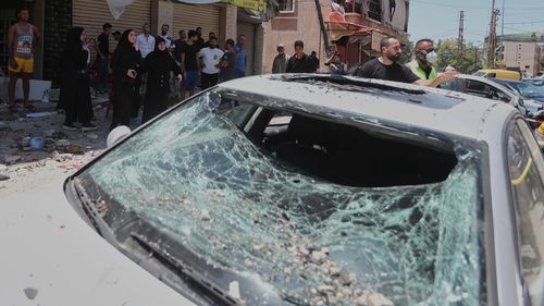 People gather next to a car that was damaged in an Israeli airstrike in Nabatieh town, south Lebanon, Friday, June 27, 2025. (AP Photo/Mohammed Zaatari)