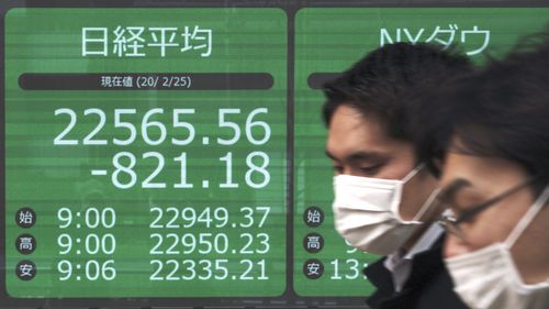 Men walk past an electronic stock board showing Japan's Nikkei 225 index at a securities firm in Tokyo.