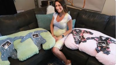 Ashley Ness sitting on the couch with four onesies laid out, two blue and two pink, with ultrasound pictures on top.