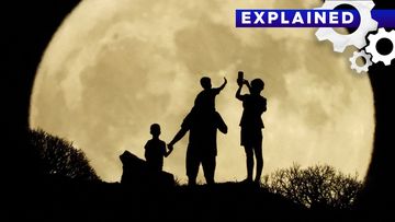 A family stand with the full moon known as the &quot;Sturgeon Moon&quot; in the background