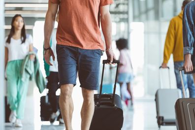 Multiracial passengers walking with wheeled luggage at airport.