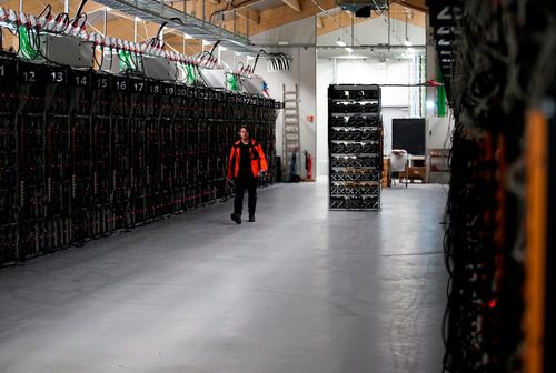 A worker walks along a row of computer rigs that run around the clock 'mining' Bitcoin inside the Genesis Mining cryptocurrency mine in Keflavik, Iceland.