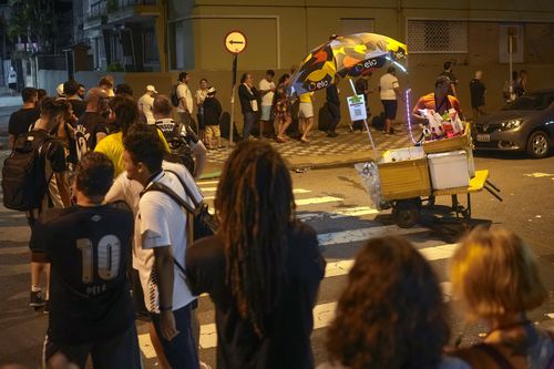 A street vendor sells drinks as soccer fans line up to attend the funeral of the late Brazilian soccer legend Pele at the Vila Belmiro stadium in Santos, Brazil, early Tuesday, Jan. 3, 2023 