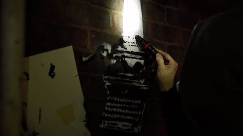 The video then cuts to Banksy as he creates the artwork on the wall of Reading Prison. 