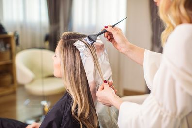 Blonde woman dyeing her hair at the salon. She is sitting and the hairdresser/hairstylist is putting hair color on her hair. This is regular hair care treatment in customers favorite salo