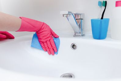 A person wearing pink gloves cleans a bathroom sink with a blue cloth, emphasizing cleanliness and hygiene.
