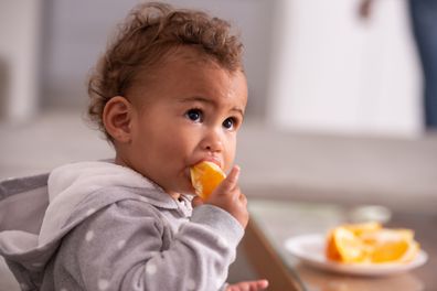 Portrait of hungry baby eating orange fruit. Child healthy eating.