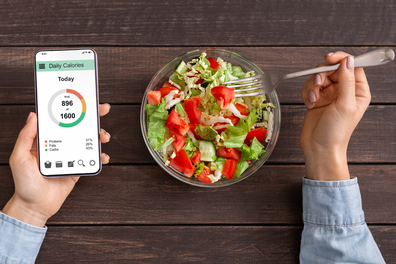 Woman counting calories on app and eating a salad