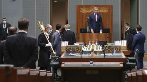 A Serjeant-at-Arms of the House of Representatives wearing a mask enters the chamber with the mace at the start of Parliament.