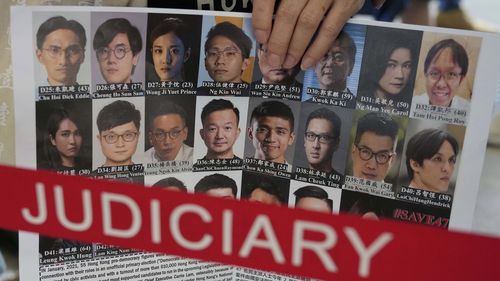 FILE - A supporter holds a banner with photos of some of the 47 pro-democracy defendants outside a court in Hong Kong on July 8, 2021. (AP Photo/Kin Cheung, File)