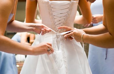 Bridesmaids doing up bride wedding dress